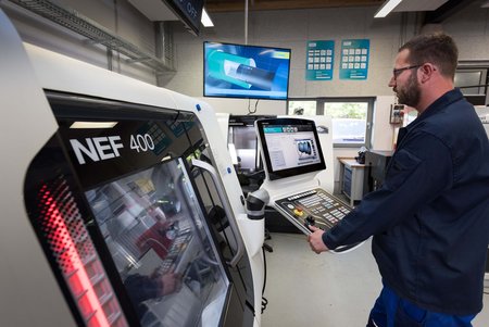 Ein Mann arbeitet in einer modernen Werkstatt an einer computergesteuerten Werkzeugmaschine mit Bildschirmen