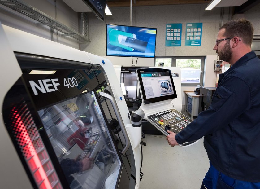 Ein Mann arbeitet in einer modernen Werkstatt an einer computergesteuerten Werkzeugmaschine mit Bildschirmen